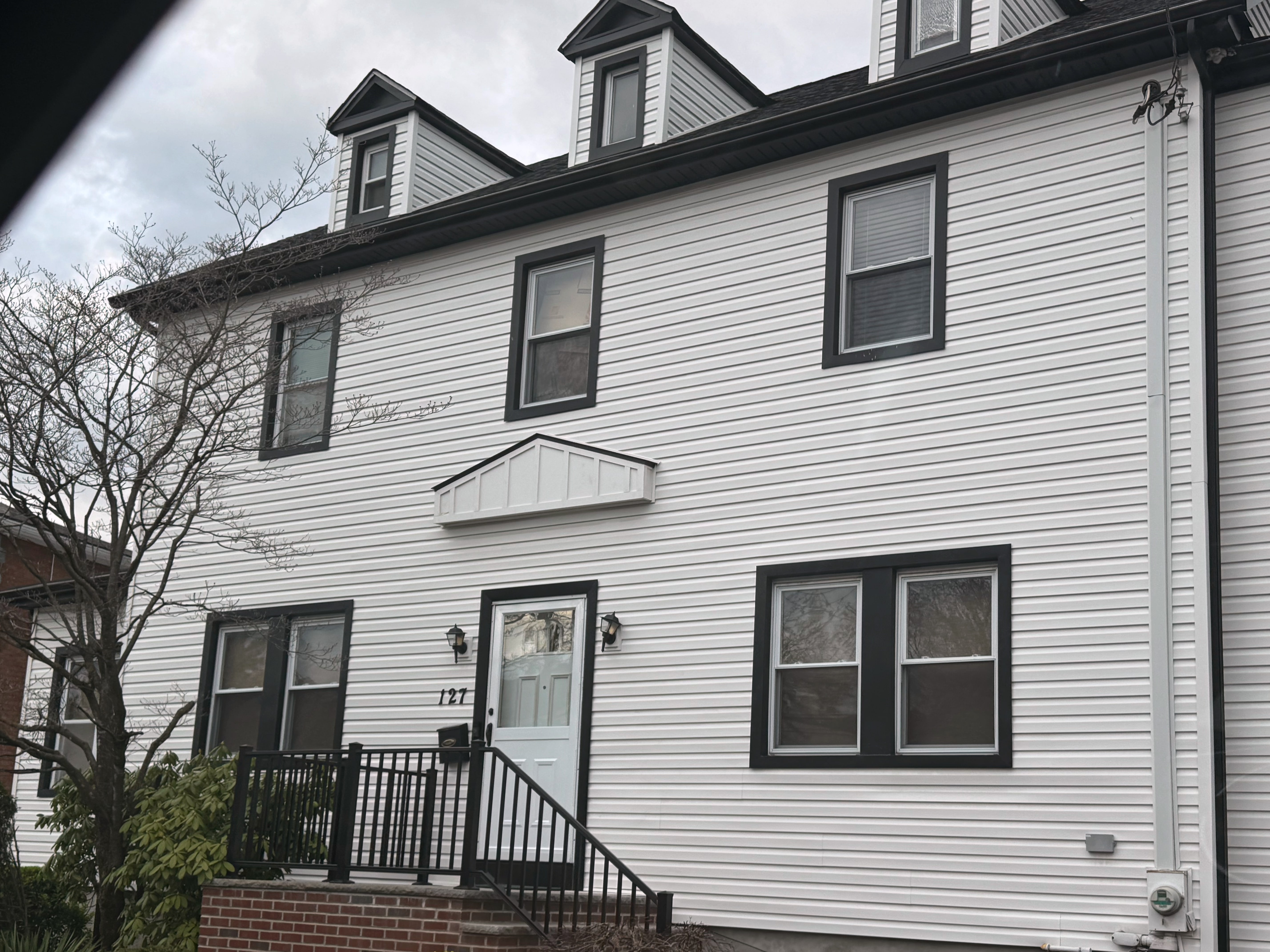 White vinyl-sided three-story house with dark trim and dormers